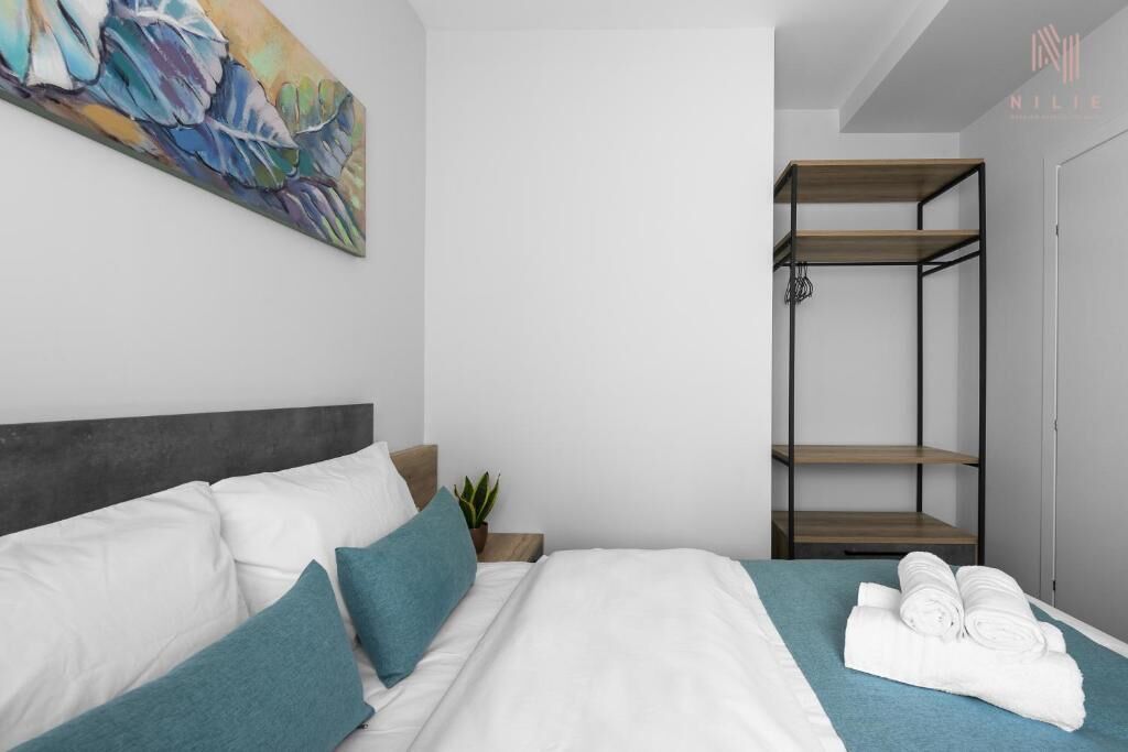 Et moderne hotelværelse med seng, et maleri, en reol i træ og en plante.