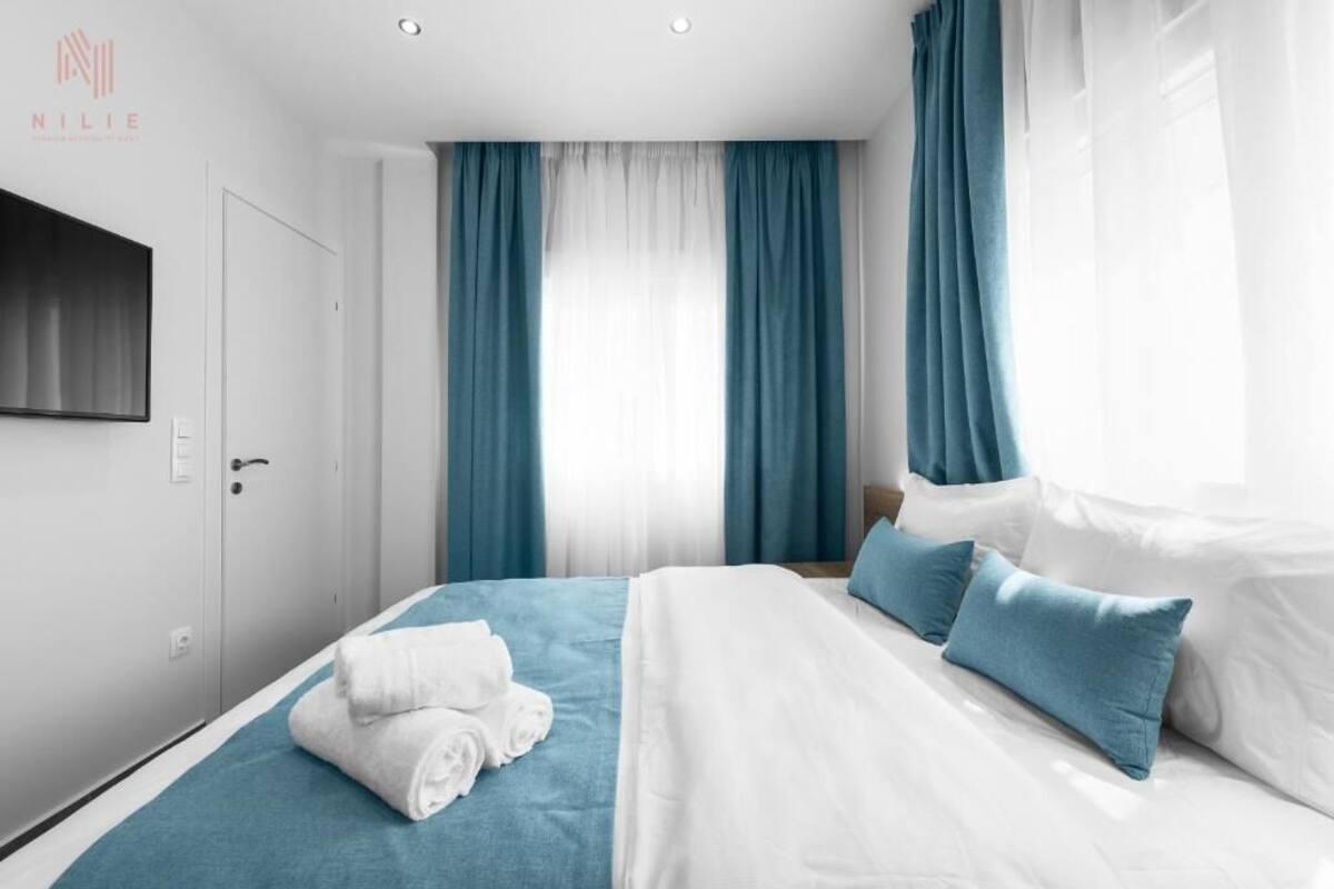 Une chambre d’hôtel avec un lit, des rideaux bleus, un téléviseur fixé au mur et une porte.