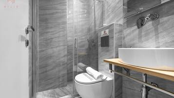 Un baño moderno con ducha de vidrio, inodoro blanco y tocador de madera con lavamanos.