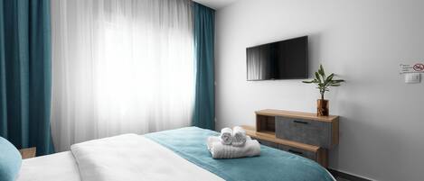 A modern hotel room with a bed, a flat-screen TV, a wooden nightstand, and a potted plant.