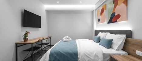 Une chambre d’hôtel moderne équipée d’un lit, d’une table de chevet, d’un bureau, d’une chaise et d’un téléviseur à écran plat.