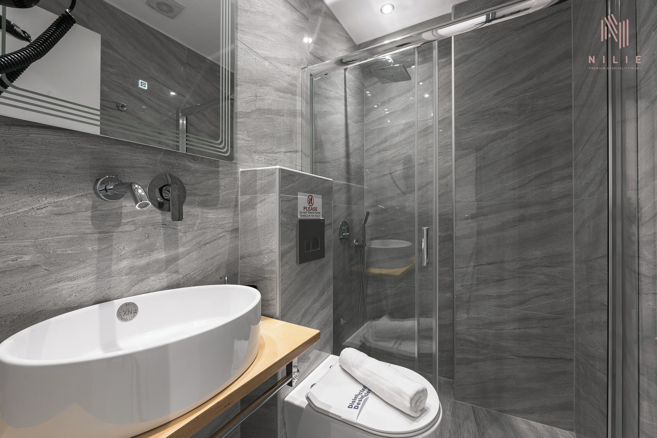 A modern bathroom with a large white sink, a glass shower enclosure, and a toilet with a towel on it.