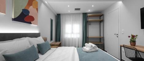 A modern hotel room with a neatly made bed, a desk with a chair, a wardrobe, and a large abstract painting on the wall.
