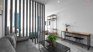 A modern living room with a sofa, a coffee table with a plant, a desk with two chairs, and a sliding door with vertical blinds. - Factory Inn Nilie Hospitality MGMT (Thessaloniki)