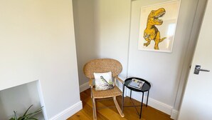A corner room with a wicker chair, a small table with a magazine, and a framed dinosaur picture on the wall. - Old Town Trinity Apartment No 4 by Adliv (Margate)