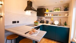 A modern kitchen with a central island, bar stools, a black range hood, and teal cabinetry. - Old Town Trinity Apartment No 4 by Adliv (Margate)