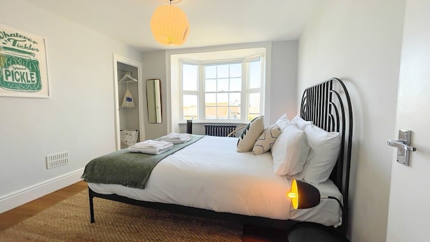 A neatly made bed with pillows and a blanket, a window with a view, a hanging bag, and a wall sign. - Old Town Trinity Apartment No 4 by Adliv (Margate)