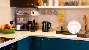 A modern kitchen with teal cabinets, a coffee machine, a kettle, and a fruit bowl. - Old Town Trinity Apartment No 4 by Adliv (Margate)