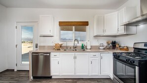 Una cocina moderna con armarios blancos, un lavavajillas de acero inoxidable, una estufa a gas y una ventana con vistas a montañas.