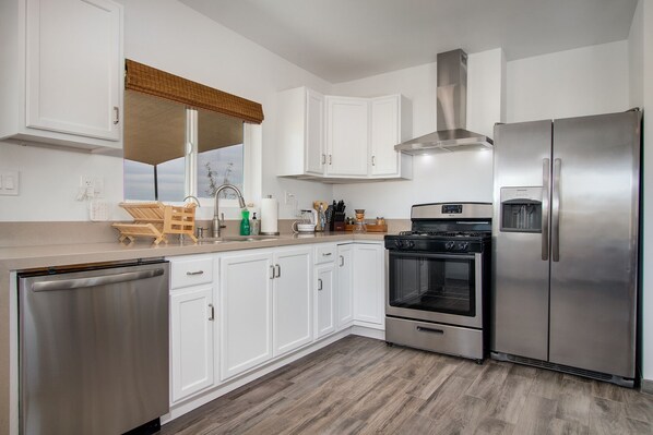 A modern kitchen with white cabinets, stainless steel appliances, and a wooden floor.