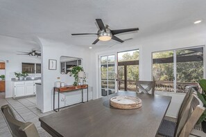 Eine geräumige Küche mit weißen Schränken, ein Essbereich mit einem Holztisch und ein Deckenventilator.