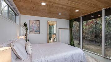 Una camera da letto con un'ampia finestra, soffitto in legno e un letto con biancheria bianca.