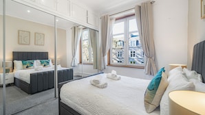 A modern hotel room with a large bed, a bedside table, a mirror, and a window with curtains.