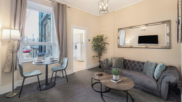 A modern living room with a sofa, coffee table, and chairs, a television, and a large window with curtains.