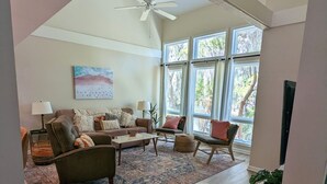 Ein geräumiges Wohnzimmer mit großem Fenster, Deckenventilator und einer gemütlichen Sitzecke.