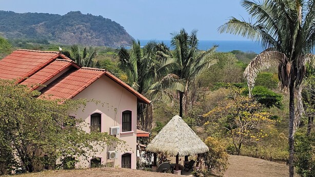 A house with a red roof, surrounded by tropical vegetation and a view of the ocean. - Great House (Guanacaste Province)