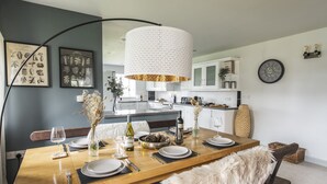 Een moderne keuken met een houten eettafel voor vier personen, een hanglamp en ingelijste botanische prints aan de muur.