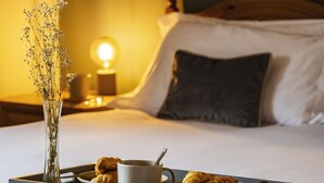 Een netjes opgemaakt bed met een dienblad met ontbijtartikelen, waaronder croissants en een beker, in een hotelkamer met een bedlamp en een bloevas.