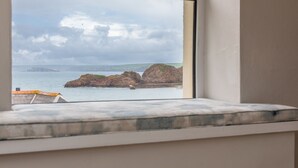 Vista desde una ventana sobre un paisaje costero con afloramientos rocosos y agua tranquila.