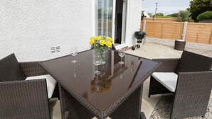 A patio with a glass-top table, wicker chairs, and a vase of yellow flowers. - White Stones (Ulverston)