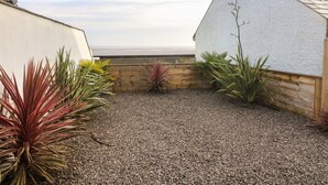 A courtyard with a gravel ground, wooden fence, and various plants. - White Stones (Ulverston)