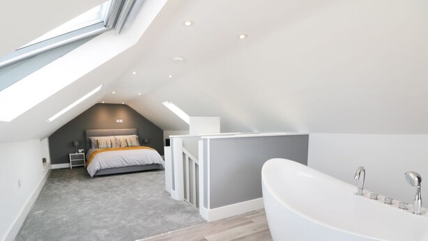 A modern bedroom with a skylight, a large bed, a walk-in closet, and a separate bathroom with a freestanding bathtub. - White Stones (Ulverston)