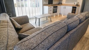 A modern living room with a sofa set, a coffee table, and a kitchen area with a microwave and oven. - White Stones (Ulverston)