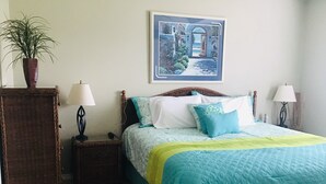 Quarto com cama, mesa de cabeceira, abajur, planta em vaso e quadro na parede.