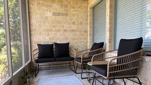 Eine überdachte Veranda mit Korbmöbeln, einem Betonboden und einer Backsteinmauer.