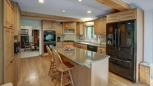A spacious kitchen with wooden cabinets, a large island with bar stools, a stainless steel refrigerator, and a dishwasher.