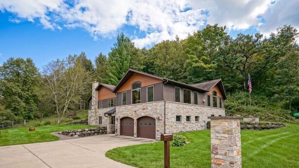 A large stone house with a stone driveway, two garages, and a well-maintained lawn.