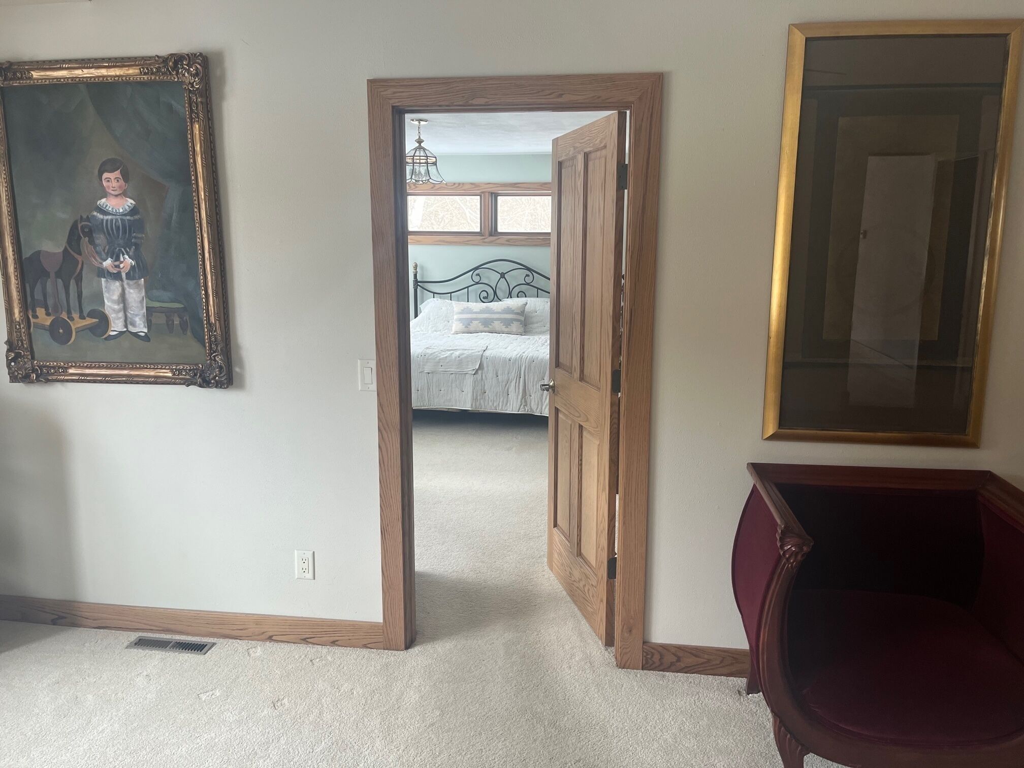 A room with a bed, a door leading to another room, a chair, and a framed picture on the wall.