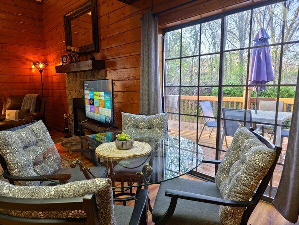 A cozy cabin interior with a TV, patterned furniture, and a deck with outdoor seating.