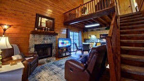 A cozy log cabin interior with a stone fireplace, leather seating, a television, and a wooden staircase. - Cozy Cabin~Sleeps 6~Great Location~Dog-Friendly (Branson)