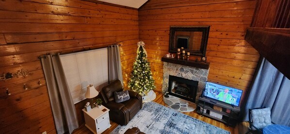 A cozy cabin interior with a fireplace, a Christmas tree, and a television.
