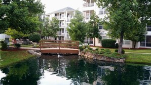 A residential area with a wooden bridge over a pond, surrounded by lush greenery and multi-story buildings. - Cozy Cabin~Sleeps 6~Great Location~Dog-Friendly (Branson)