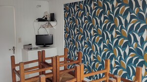 Une pièce avec un mur orné d’un motif, un téléviseur posé sur un meuble et des chaises en bois.