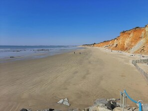 A wide sandy beach with a rocky cliff on the right and calm water in the background.