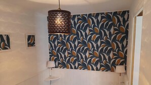 Une chambre à coucher avec un lit, deux lampes de chevet, un luminaire suspendu et un papier peint à motifs.