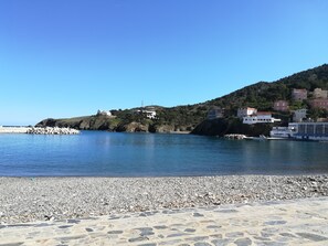 A coastal area with a pebble beach, a rocky shoreline, and buildings on a hillside.