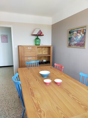 A dining area with a wooden table, blue and pink chairs, a green vase, and a framed poster on the wall.