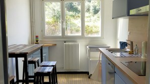 Une cuisine avec une fenêtre, un radiateur, un évier et une table avec des tabourets.