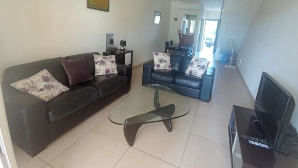 A living room with a black leather sofa, a glass coffee table, and a television on a stand. - 2 Bedroom House Sleeps 6 - Pool, Hot Tub, Garden (Mandria)