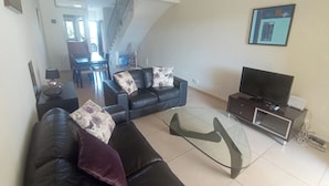 A living room with a sofa, a glass coffee table, a TV stand, and a staircase leading to another room. - 2 Bedroom House Sleeps 6 - Pool, Hot Tub, Garden (Mandria)