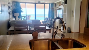 Una cucina con lavello in acciaio inossidabile, un'area pranzo con tavolo e sedie, e vista sull'oceano attraverso ampie finestre.