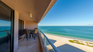 Un balcon avec une table et des chaises donnant sur une plage aux eaux turquoise et cristallines.