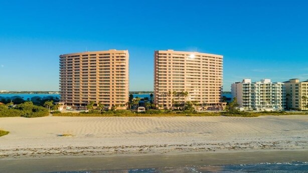 Un hotel fronte spiaggia con due edifici circolari ben visibili, una spiaggia sabbiosa in primo piano e un cielo azzurro limpido.