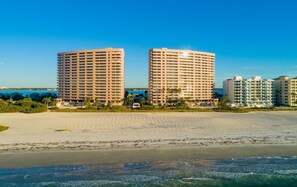 Ett hotell vid stranden med två markanta, runda byggnader, en sandstrand i förgrunden och en klarblå himmel.