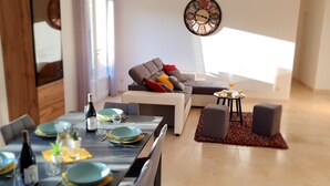 A modern living room with a sofa, a dining table set with plates and glasses, and a small table with a tray of snacks.