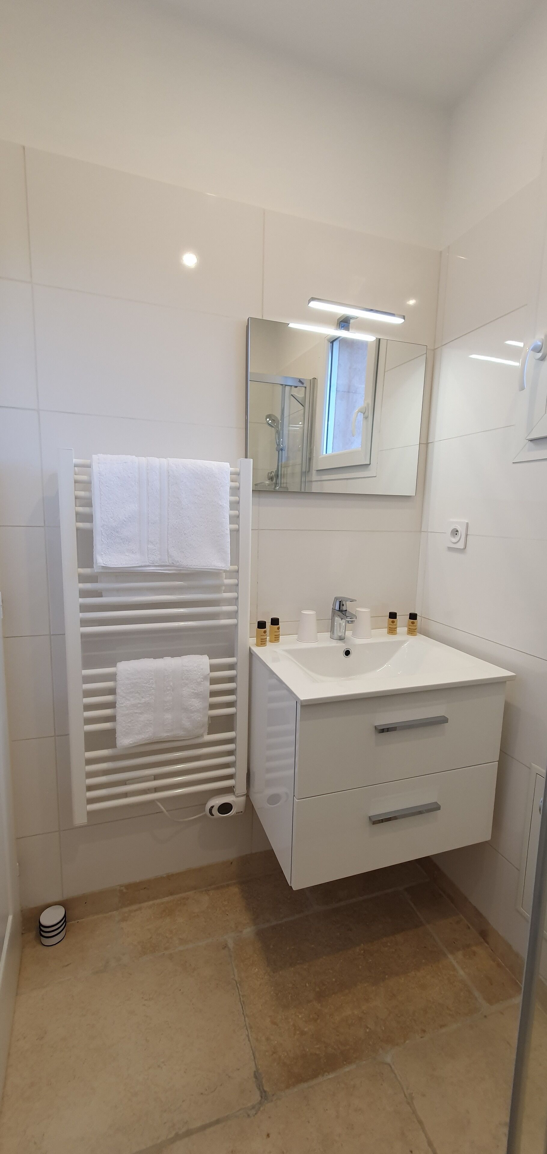 Un baño moderno con tocador blanco, perchero, espejo y zona de ducha.